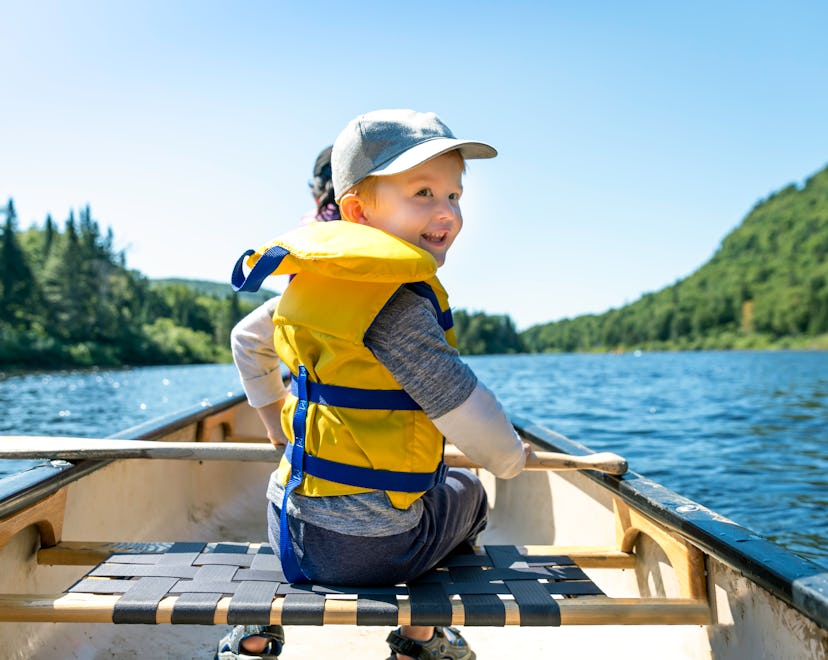 Little boy in canoe smiles over his shoulder, in a story about how to choose the best life jacket fo...