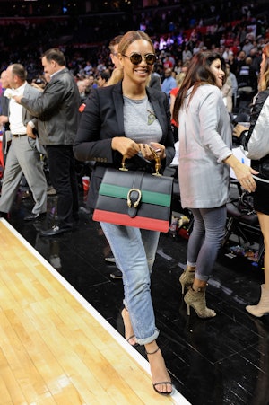Beyonce wears jeans and a blazer at a basketball game and carries a striped Gucci Dionysus bag. 
