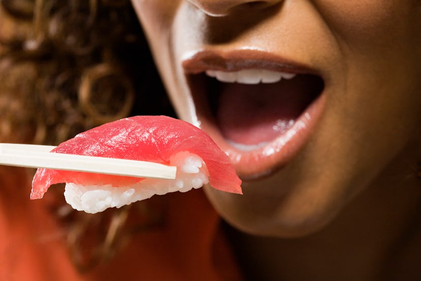 woman eating raw tuna in an article about foods to avoid while breastfeeding