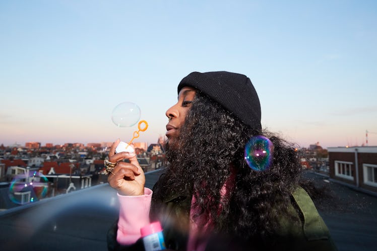 young woman blows bubbles during sunset as she considers how saturn retrograde 2023 will affect her ...