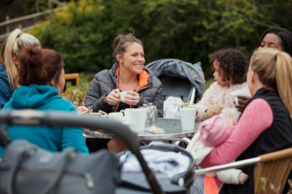 A group of mothers are sitting at a table in the park with their adorable kids having tea and coffee...
