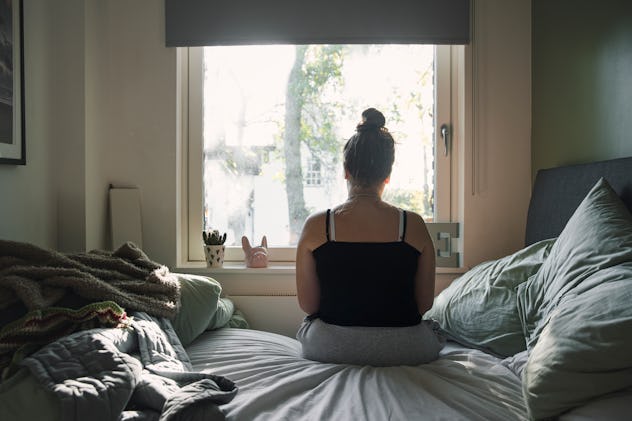 gloomy shot of woman looking out window; adrenal fatigue is a physical symptom of negative energy in...