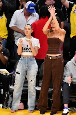 Kim Kardashian wears a graphic tee and jeans beside a friend at a basketball game. 