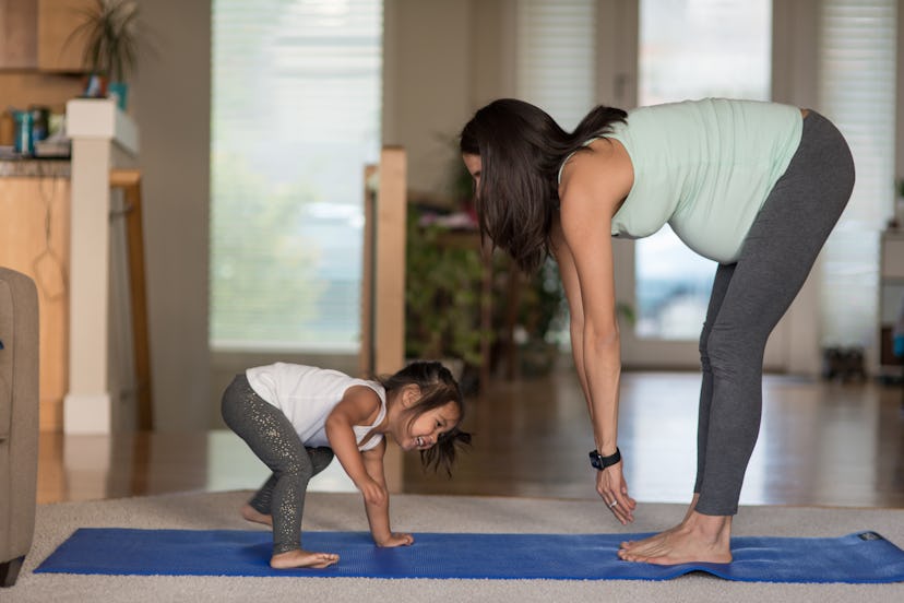 Ethnic pregnant mother doing yoga with her young toddler at home, treating her prenatal anxiety with...