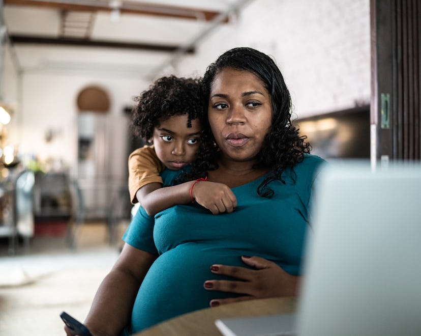 Pregnant woman using laptop at home with son, having a little uneasy feeling before labor.