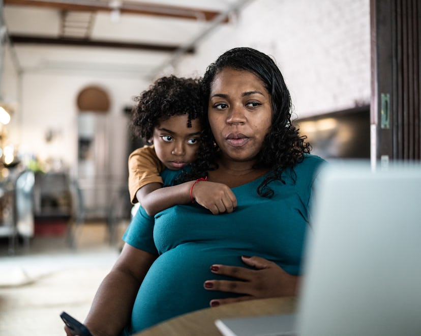 Pregnant woman using laptop at home with son, having a little uneasy feeling before labor. 