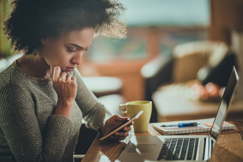 Young black woman reading on phone while working at home, in an article about miscarriage worries.