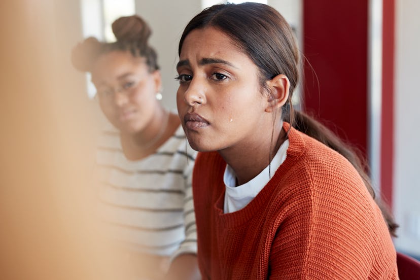 Emotionally stressed young woman crying while looking away sitting with friend during psychotherapy ...