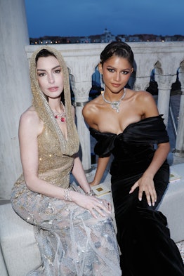 Anne Hathaway wears a gold and silver hooded dress beside Zendaya, who is in a black off-the-shoulde...