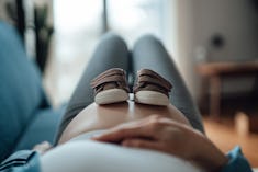 Pregnant woman putting a pair of baby shoes on her bump in an article about pelvic rest