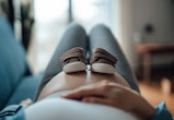 Pregnant woman putting a pair of baby shoes on her bump in an article about pelvic rest