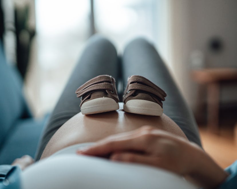 Pregnant woman putting a pair of baby shoes on her bump in an article about pelvic rest
