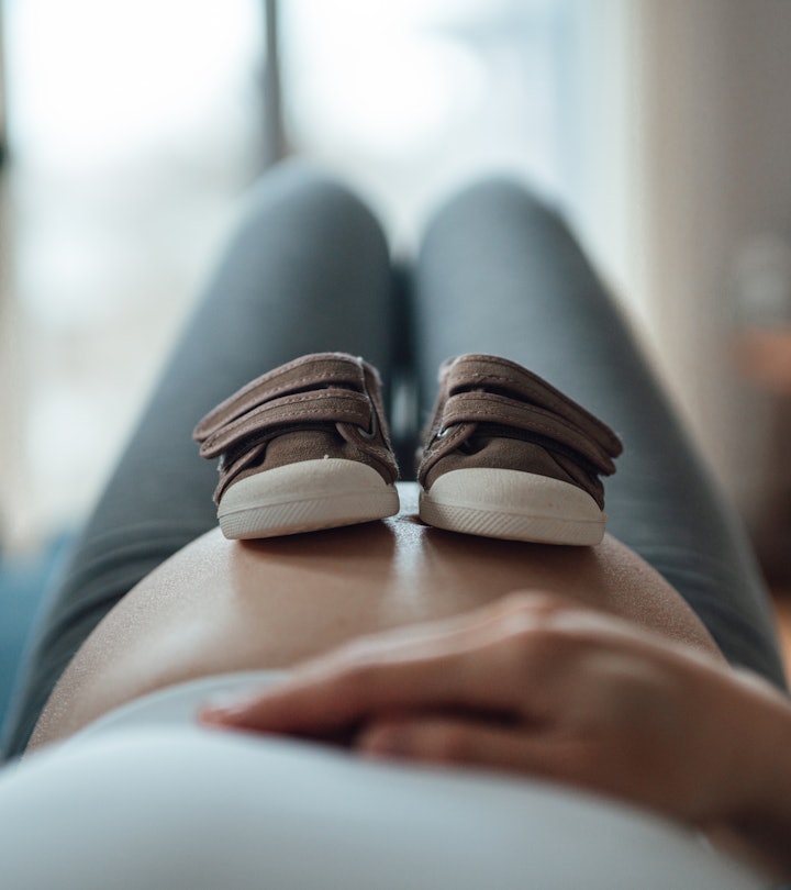 Pregnant woman putting a pair of baby shoes on her bump in an article about pelvic rest