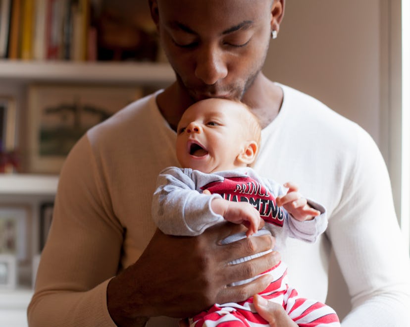 black father kissing newborn's head in article about best gifts for new dads