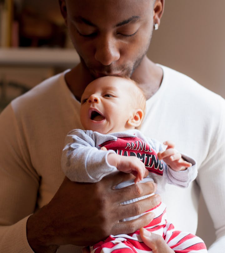 black father kissing newborn's head in article about best gifts for new dads