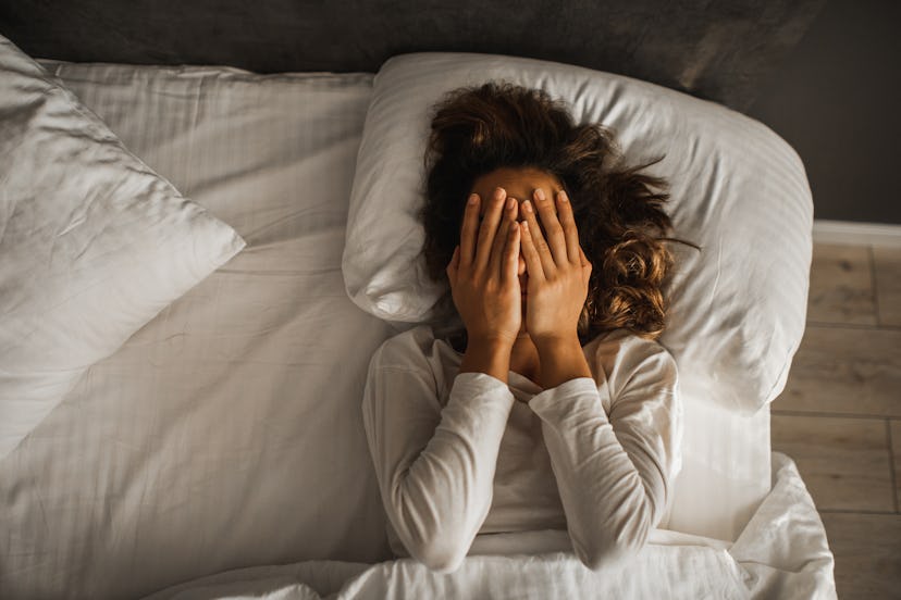 Do I have a mental health issue or PMS? Woman lays in bed and covers her face with her hands.