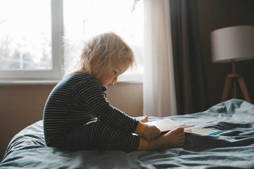 Goth baby names would be fitting for this toddler, sitting in bed reading a book.