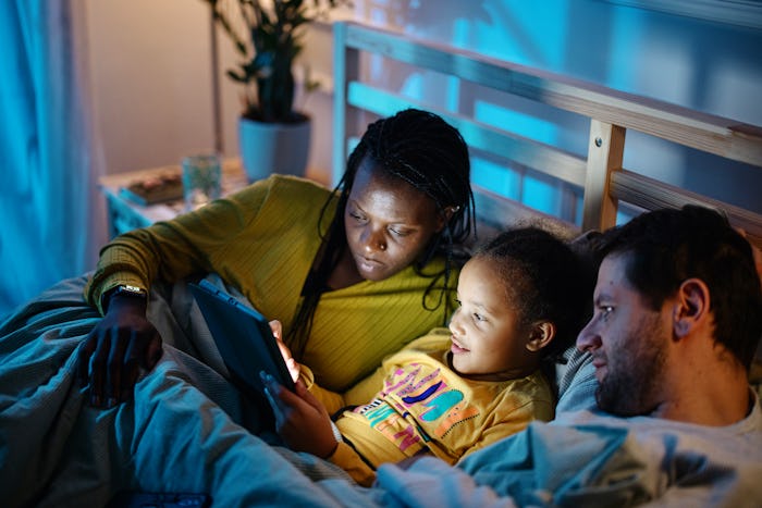 Multiethnic family using a digital tablet together in bed at night before falling asleep