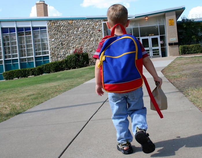 Young Elementary Schoolboy walking up to school carrying backpack and brown bag for lunch or show/t...