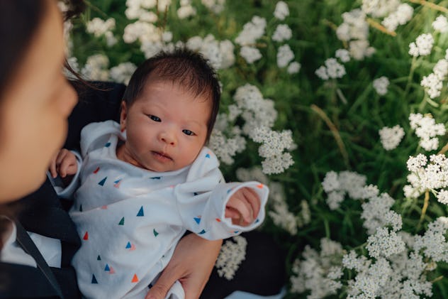May baby names would suit this newborn, held by their mom with blooming white flowers in the backgro...