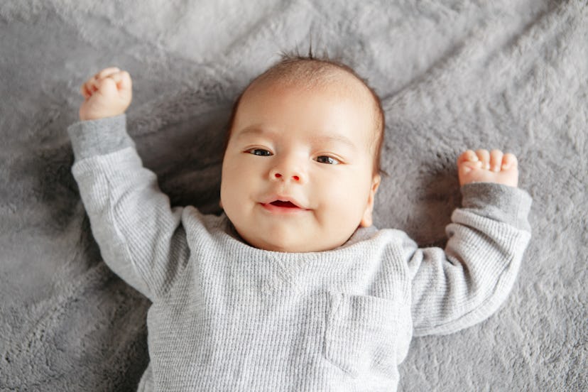 Goth baby names would be fitting for this newborn baby, grinning, wearing a gray shirt.