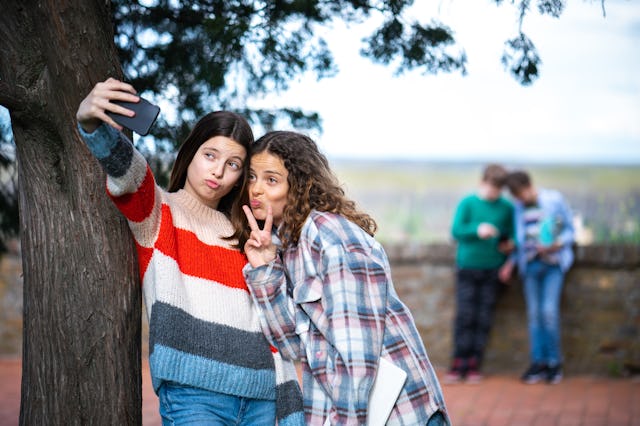 Happy teenage girls taking a selfie in park. According to new data, teens are on social media more t...