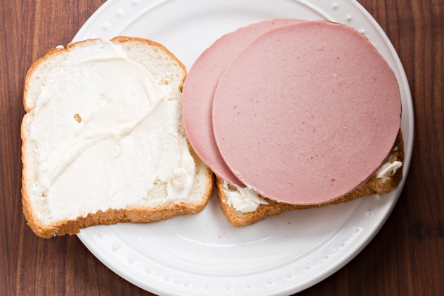 An overhead close up view of a white plate with an open face bologna sandwich on white sourdough bre...