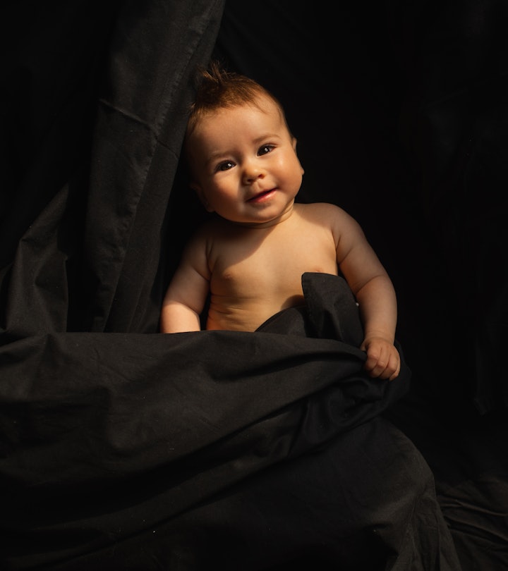 Spooky baby names would fit this baby, laying in black blankets smiling at camera.