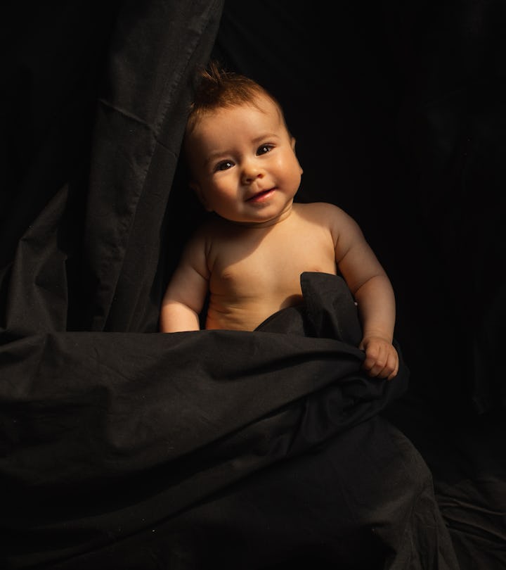 Spooky baby names would fit this baby, laying in black blankets smiling at camera.