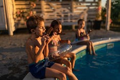 Group of small friends eating ice-cream during summer day by the pool. Focus is on boy.