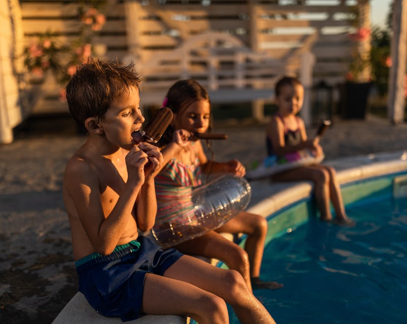 Group of small friends eating ice-cream during summer day by the pool. Focus is on boy.