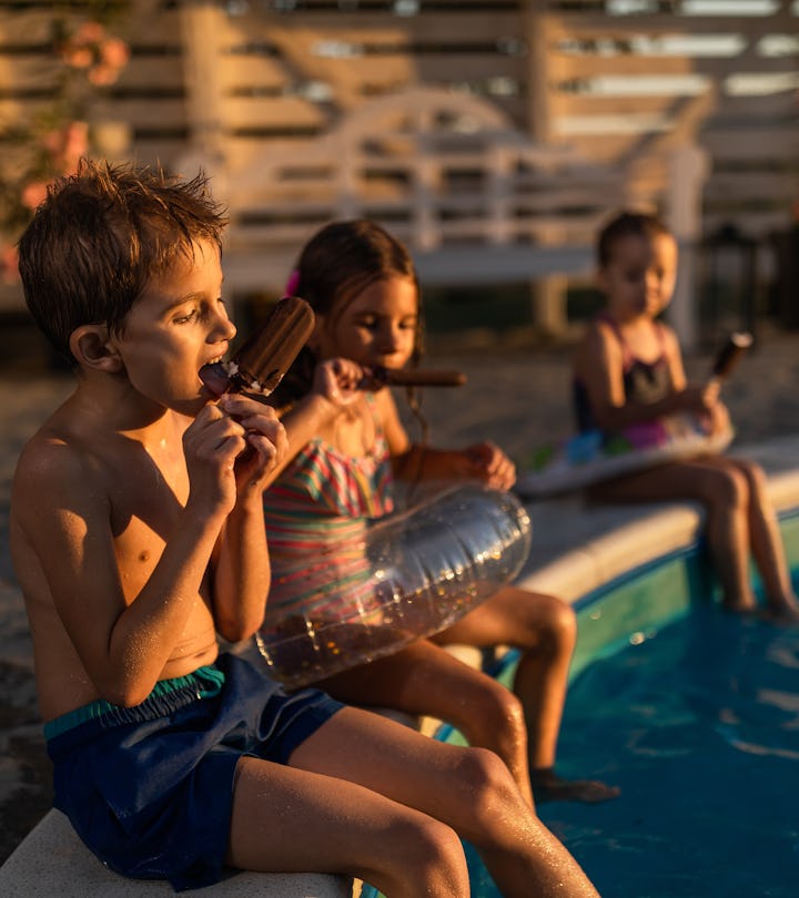 Group of small friends eating ice-cream during summer day by the pool. Focus is on boy.