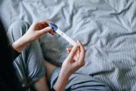 High angle view of disappointed woman sitting on bed and holding a negative pregnancy test in articl...