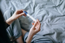 High angle view of disappointed woman sitting on bed and holding a negative pregnancy test in articl...