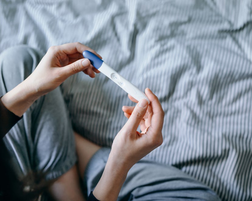 High angle view of disappointed woman sitting on bed and holding a negative pregnancy test in articl...