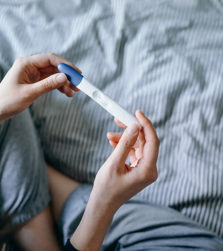 High angle view of disappointed woman sitting on bed and holding a negative pregnancy test in articl...