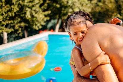 Man comforting his upset daughter at swimming pool