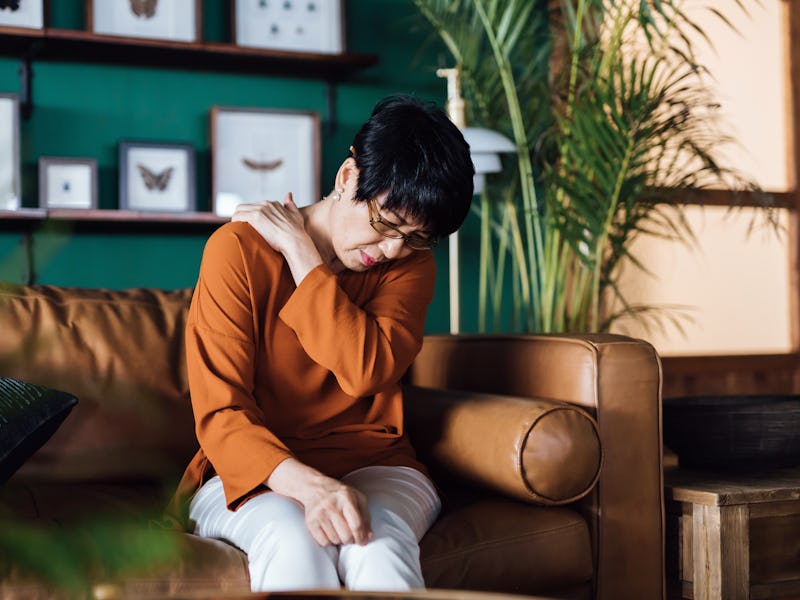 A distraught senior Asian woman feeling unwell, suffering from neck and shoulder pain, massaging ach...