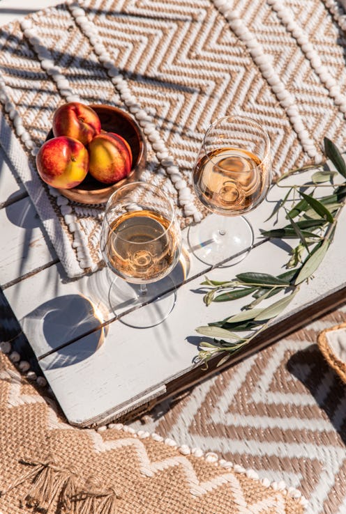 Drinking rose wine glasses on white wood table with peaches on sunny mediterranean day