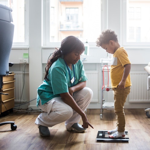 A boy steps on a scale, as directed by a healthcare worker.