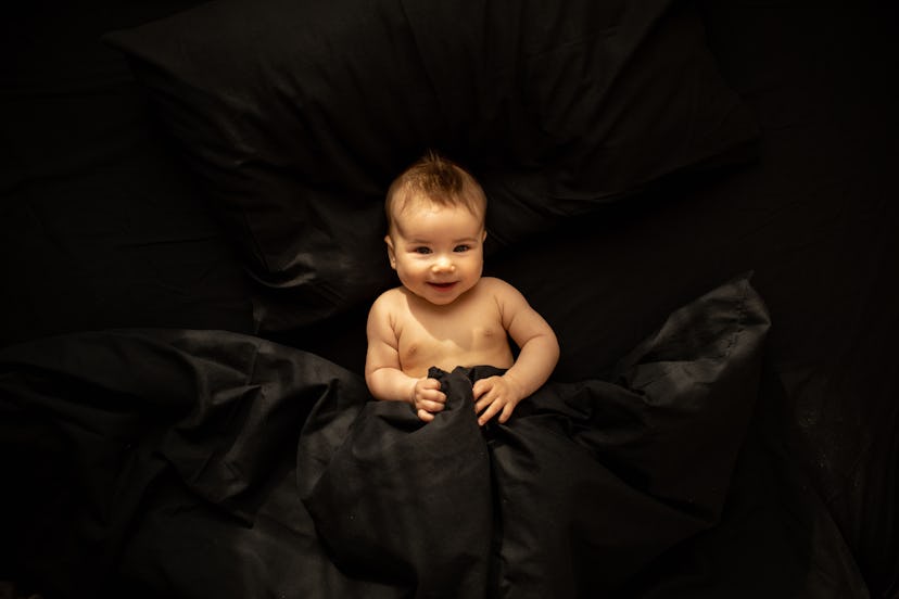 Goth baby names would fit this adorable smiling baby surrounded in black sheets.