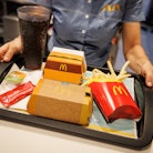 02 December 2021, Bavaria, Munich: An employee hands over a tray with French fries, a Coca Cola, ket...
