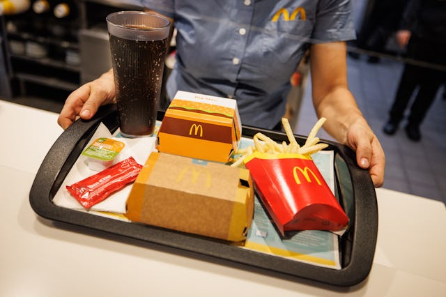 02 December 2021, Bavaria, Munich: An employee hands over a tray with French fries, a Coca Cola, ket...