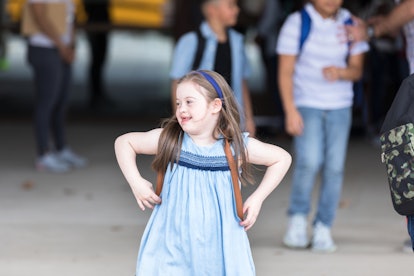 An elementary age girl with Down Syndrome smiles as she gets off of school bus. She is excited about...
