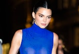 Kendall Jenner wears a blue sleeveless dress with feathers and carries a matching blue bag. 