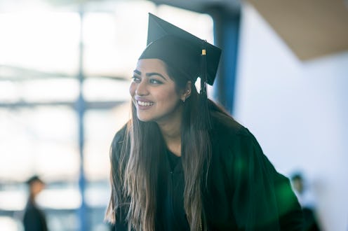 A female University graduate poses for an individual portrait after the ceremony. She is dressed in...