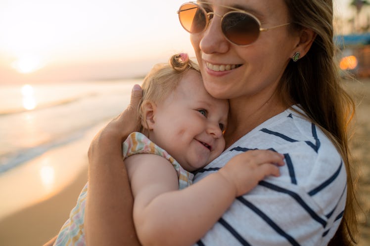 A mother holding her baby to her chest on a beach.