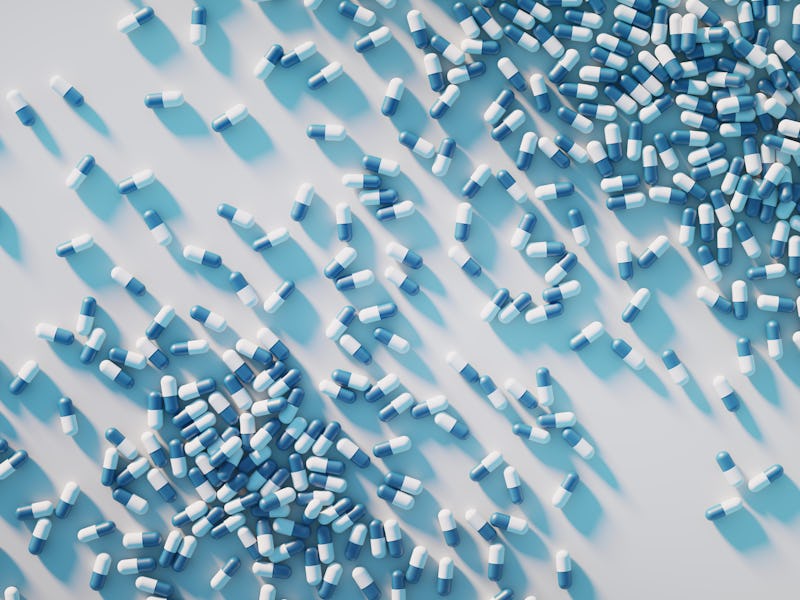 White and blue capsule pills on a white background. A large group of pills are scattered over a whit...