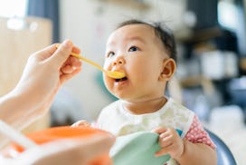 When can babies eat eggs? Baby takes a spoonful of food from a parent out of frame.