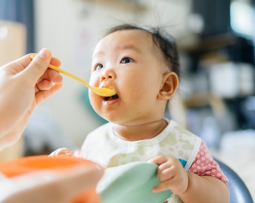 When can babies eat eggs? Baby takes a spoonful of food from a parent out of frame.